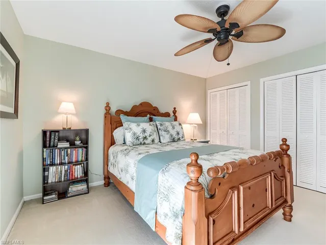 Bedroom with two closets, light colored carpet, and a ceiling fan