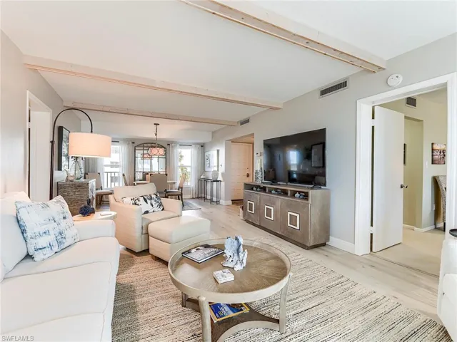 Living room featuring beamed ceiling, light wood-style flooring, and a chandelier