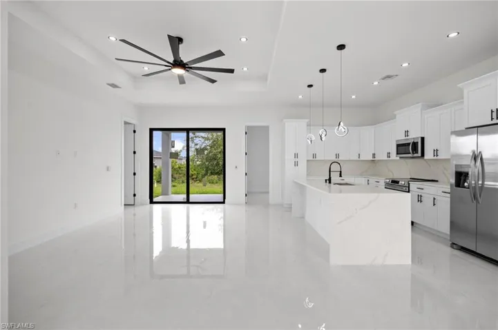 Open-concept living space featuring high-gloss tile flooring, a modern kitchen island with integrated sink, stainless steel appliances, and sleek white cabinetry