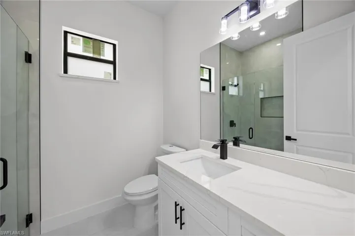 Modern bathroom featuring a white vanity with a quartz countertop and integrated sink, matte black faucet, and frameless mirror