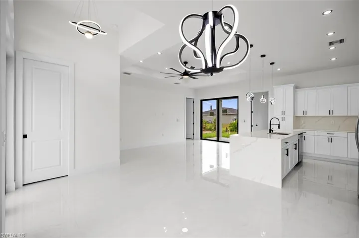 Open-concept living area featuring a modern kitchen island with waterfall countertop, white cabinetry with black hardware, and sleek pendant lighting
