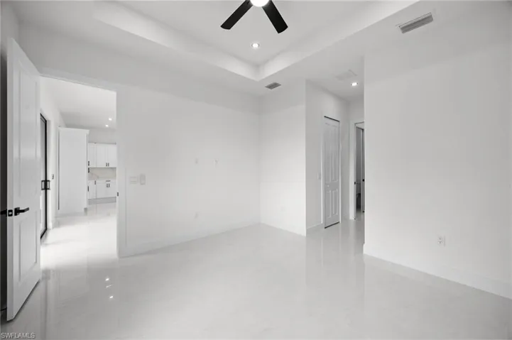 Spacious room featuring white tile flooring, white walls, a tray ceiling with recessed lighting, and a contemporary ceiling fan