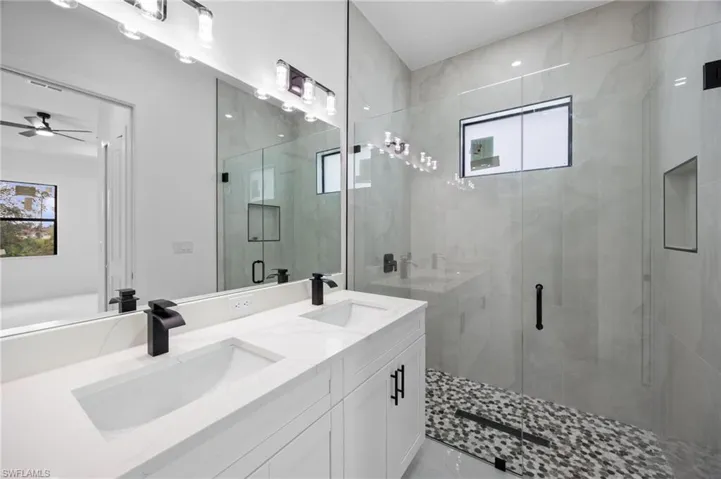 Contemporary bathroom featuring a dual vanity with white cabinetry and integrated sinks, matte black fixtures, and a frameless glass shower enclosure