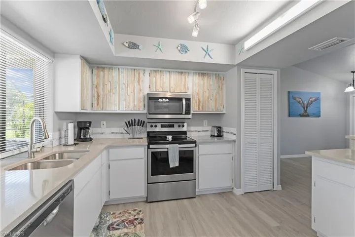 Kitchen with appliances with stainless steel finishes, light countertops, light wood-type flooring, track lighting, and white cabinets
