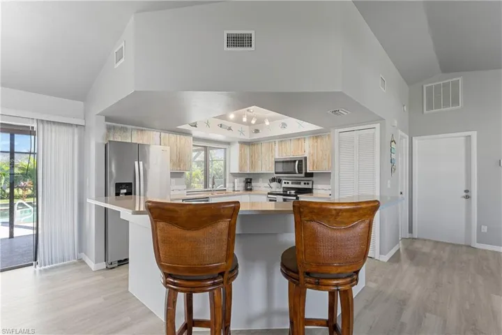 Kitchen with appliances with stainless steel finishes, light wood-style floors, light countertops, a breakfast bar, and high vaulted ceiling