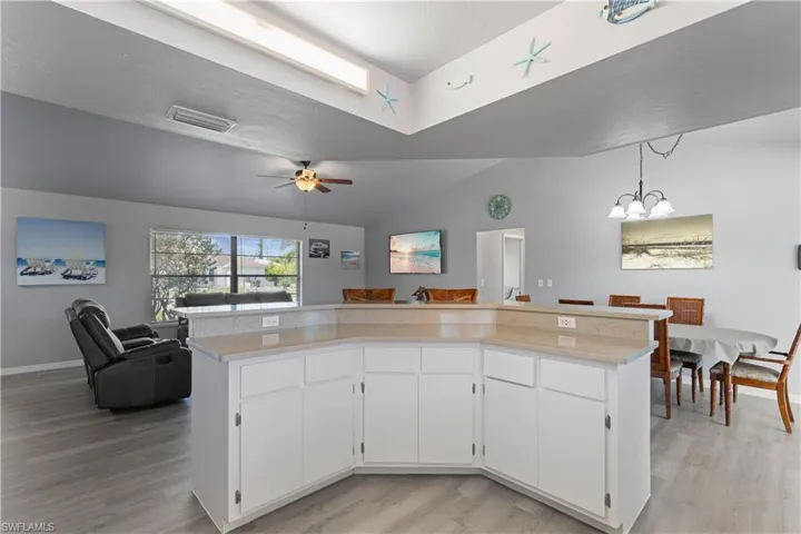 Kitchen featuring light wood-type flooring, open floor plan, light countertops, vaulted ceiling, and white cabinets