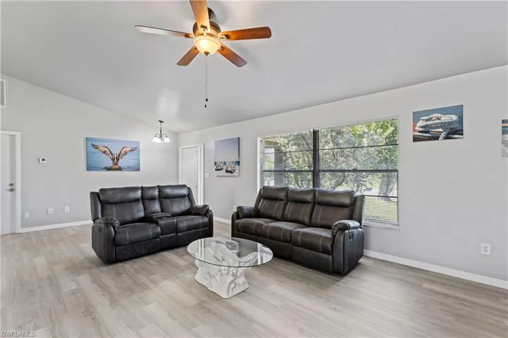 Living area featuring vaulted ceiling, light wood finished floors, ceiling fan, and a chandelier