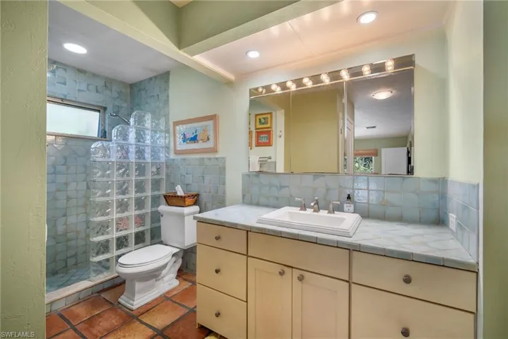 Bathroom with a tile shower, tasteful backsplash, tile patterned flooring, toilet, and vanity
