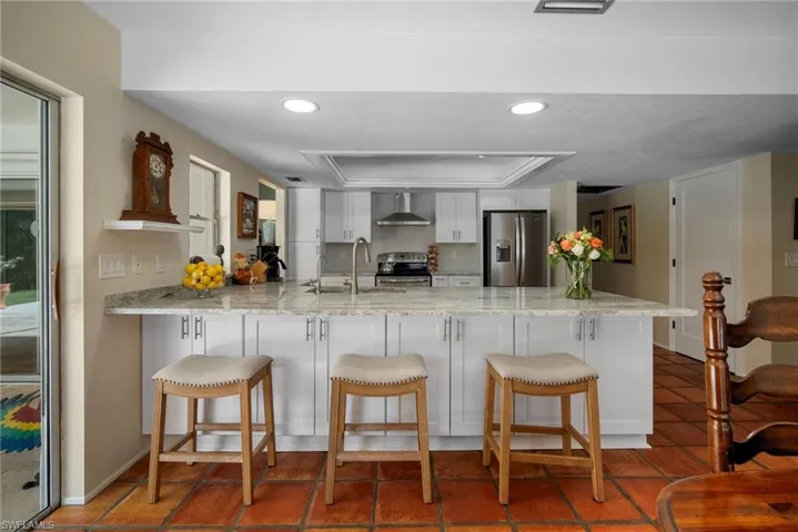 Kitchen featuring a kitchen bar, kitchen peninsula, stainless steel appliances, and wall chimney range hood