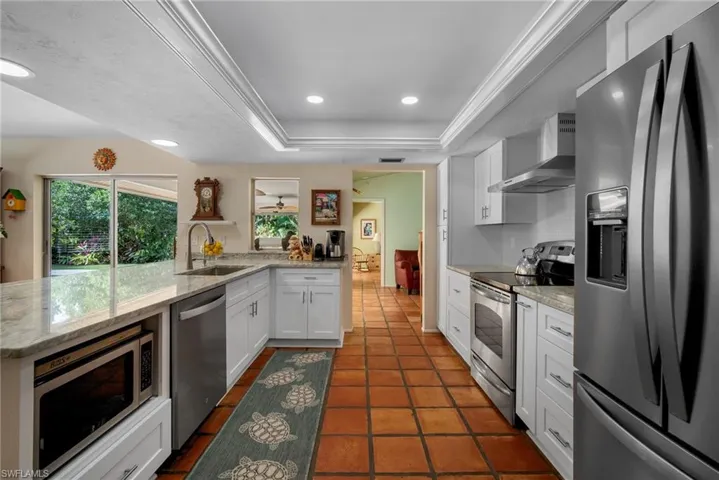 Kitchen with wall chimney exhaust hood, stainless steel appliances, a tray ceiling, sink, and white cabinetry
