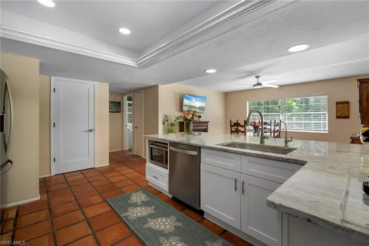 Kitchen with light stone countertops, ceiling fan, sink, stainless steel appliances, and white cabinets