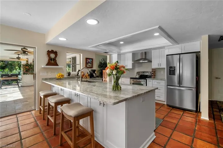 Kitchen with white cabinetry, wall chimney range hood, kitchen peninsula, a breakfast bar area, and appliances with stainless steel finishes