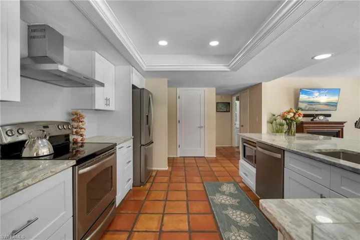 Kitchen featuring appliances with stainless steel finishes, white cabinetry, a raised ceiling, and wall chimney range hood