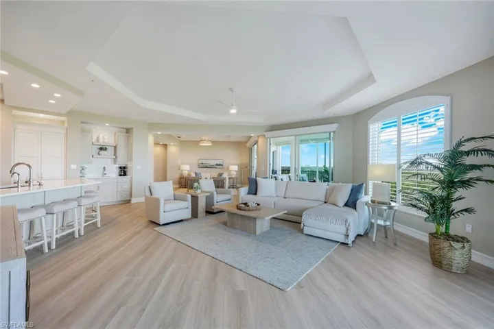 Living area featuring a tray ceiling, light wood finished floors, baseboards, ceiling fan, and recessed lighting