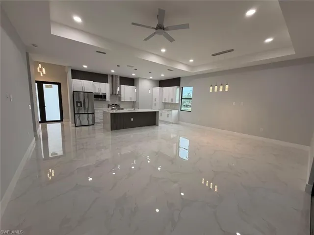 Unfurnished living room with a raised ceiling, a ceiling fan, recessed lighting, and light marble finish floors