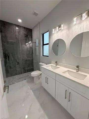 Full bathroom with double vanity, a marble finish shower, light marble finish floors, and recessed lighting