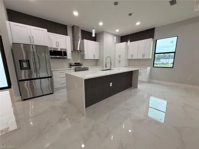 Kitchen with appliances with stainless steel finishes, light stone countertops, pendant lighting, white cabinets, and wall chimney range hood