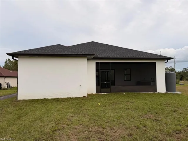 Rear view of house featuring a sunroom, a lawn, a shingled roof, and stucco siding