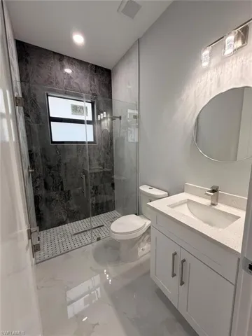 Full bath with vanity, a marble finish shower, and marble tiled floors