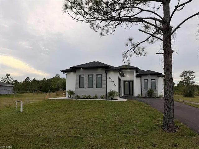 Prairie-style house with a front yard, driveway, stucco siding, and a shingled roof