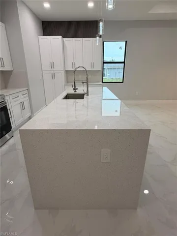 Kitchen with light stone countertops, light marble finish flooring, a large island with sink, decorative light fixtures, and recessed lighting