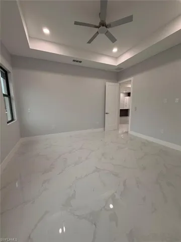 Empty room with a raised ceiling, light marble finish flooring, recessed lighting, and ceiling fan