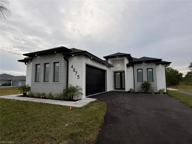 Prairie-style home with driveway, stucco siding, a front yard, and an attached garage