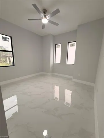 Spare room with light marble finish flooring, plenty of natural light, and ceiling fan
