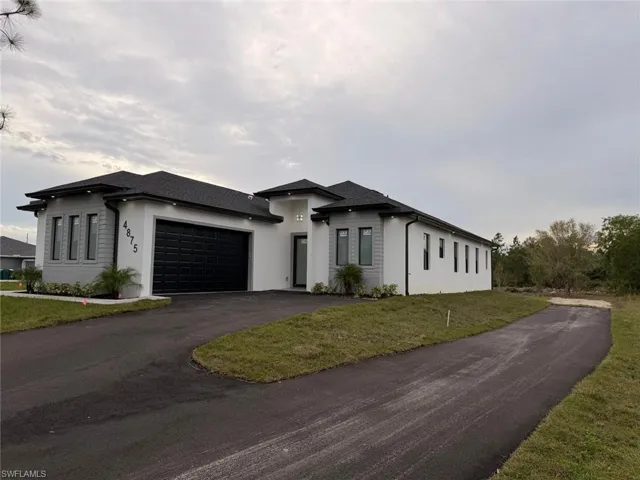 Prairie-style home featuring asphalt driveway, an attached garage, a front yard, and roof with shingles