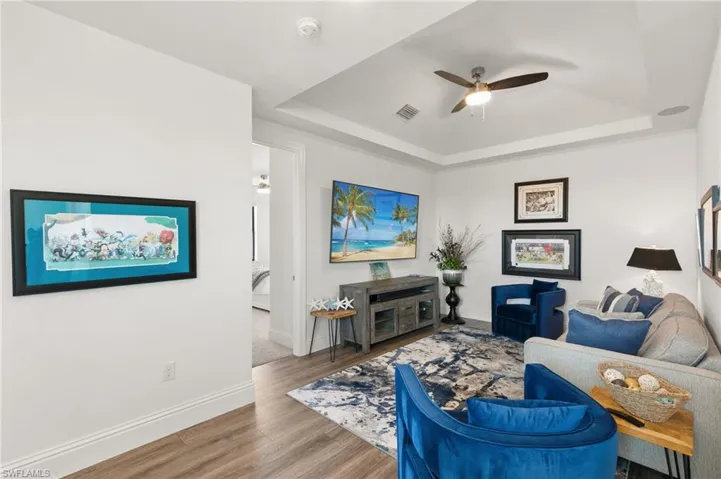 Living room with ceiling fan, wood finished floors, and a raised ceiling