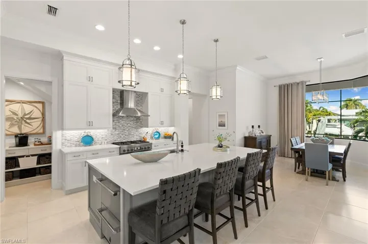 Kitchen featuring white cabinets, crown molding, backsplash, pendant lighting, and a kitchen island with sink