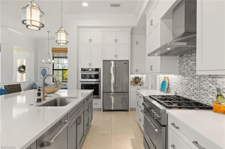 Kitchen featuring premium appliances, wall chimney exhaust hood, white cabinets, ornamental molding, and recessed lighting