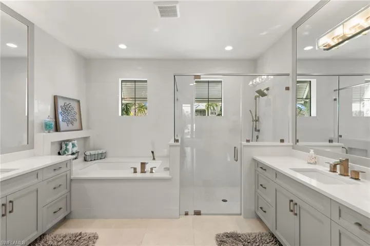 Full bathroom with two vanities, a garden tub, a stall shower, and recessed lighting
