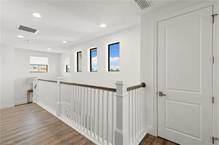 Hallway with an upstairs landing, dark wood-style floors, and recessed lighting