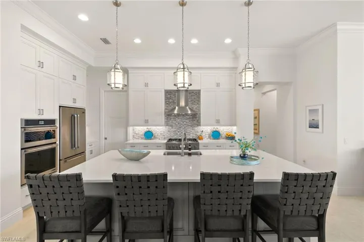 Kitchen with decorative backsplash, white cabinets, stainless steel appliances, wall chimney range hood, and recessed lighting