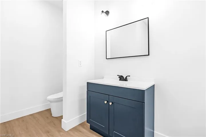 Bathroom featuring a dark blue vanity with white countertop, black-framed mirror, matte black faucet, and wood-finish flooring