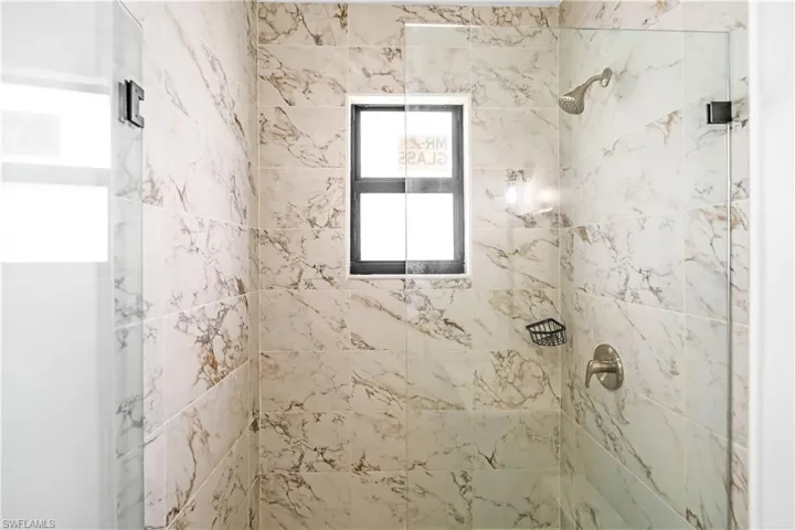 Shower with marble-look tile walls, brushed nickel fixtures, a built-in soap dish, and a clear glass enclosure