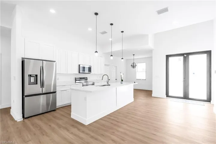 Open-concept kitchen featuring an island with a sink, white cabinetry, stainless steel appliances, and wood-finish flooring