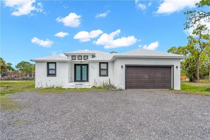 Contemporary single-story residence featuring a white stucco exterior, grey metal roof, and dark-framed windows