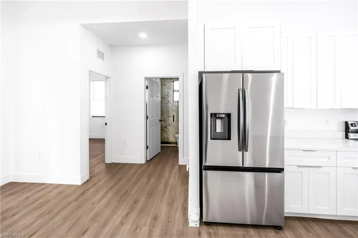 Kitchen area featuring wood-finish flooring, white shaker cabinetry, and a stainless steel French door refrigerator with an ice and water dispenser