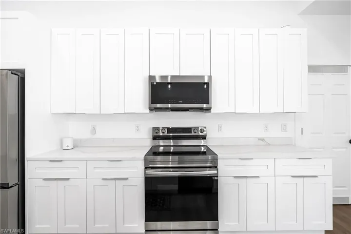 Modern kitchen featuring white shaker cabinetry, stainless steel appliances, light-toned countertops, and a full suite of upper and lower storage
