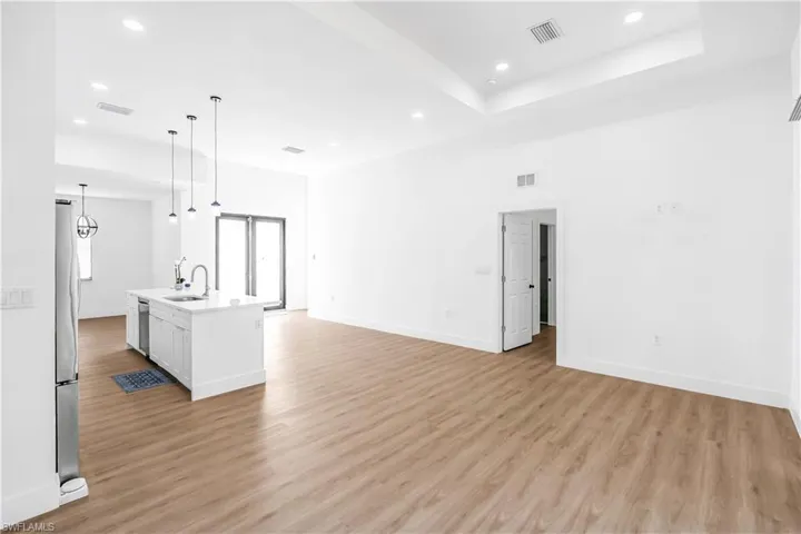 Open-concept living space featuring wood-finish flooring, recessed lighting, and a tray ceiling