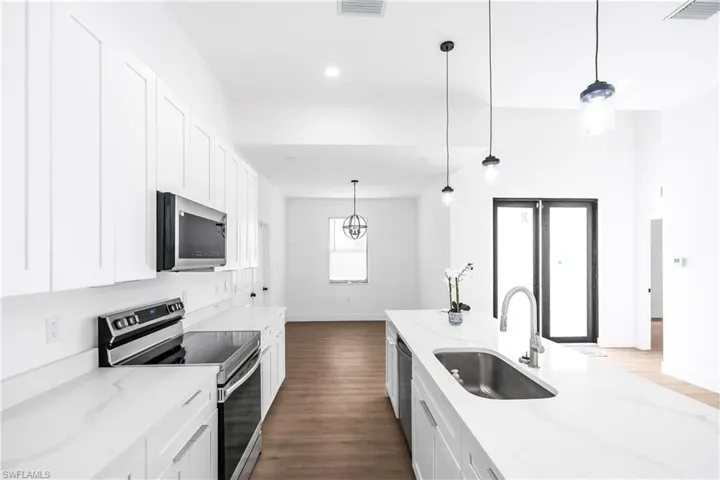 Bright kitchen featuring white shaker cabinetry, stainless steel appliances, quartz countertops, and a central island with an undermount sink and pendant lighting