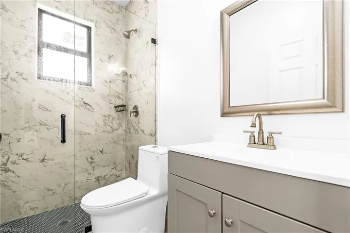 Contemporary bathroom featuring a walk-in shower with glass enclosure, marble-patterned tile, and a built-in window