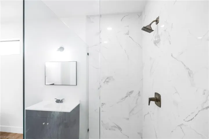Bathroom featuring a glass-enclosed shower with large format marble-look tile, a rainfall showerhead, and dark bronze fixtures