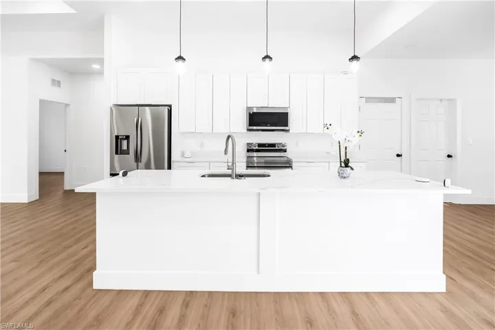 Modern kitchen featuring a large center island with integrated sink, white cabinetry, stainless steel appliances, and sleek pendant lighting