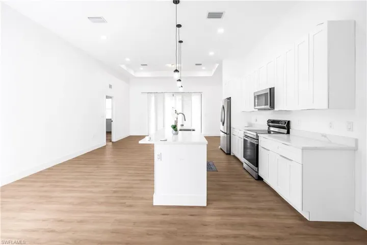 Open-concept kitchen and living area featuring wood-finish flooring, white shaker cabinetry, stainless steel appliances, a kitchen island with seating, and recessed lighting