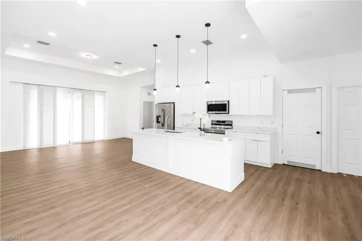 Open-concept kitchen and living area featuring wood-finish flooring, white cabinetry, a kitchen island with sink, stainless steel appliances, and tray ceiling with recessed lighting