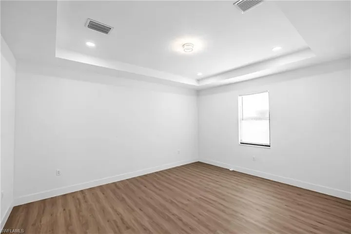 Spacious room featuring wood-finish flooring, white baseboards, and a single window with blinds