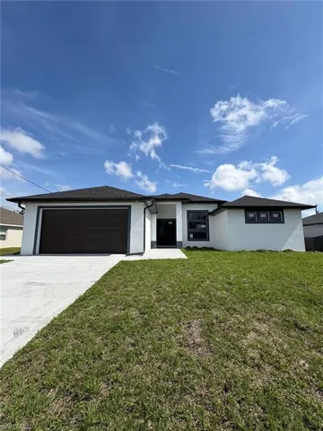 View of front facade featuring a garage, a front yard, driveway, and stucco siding